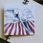 Growing Paper Dog On The Bed Greeting Card on a book showing scale