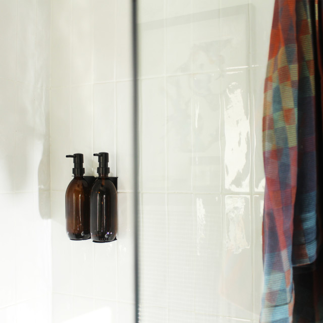 Joon Matte Black Adjustable Dispenser with Amber Bottle - Double on a wall in the shower