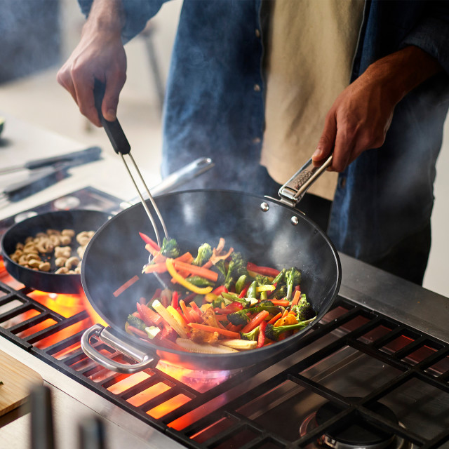Joseph Joseph Space Ceramic Non-Stick Blue Wok with Folding Handle, 32cm on the stove with stir fry