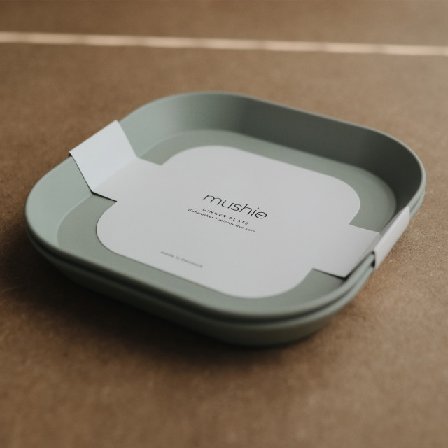 Mushie Square Dinner Plate - Sage packaging on the table