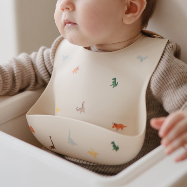 Mushie Silicone Baby Bib - Dinosaurs on a baby