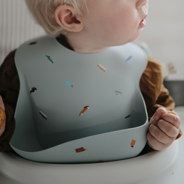 Mushie Silicone Baby Bib - Retro Cars worn by a baby