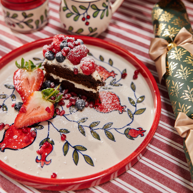 Humble & Mash Pomegranate Ceramic Platter, 25cm on a table with a slice of cake