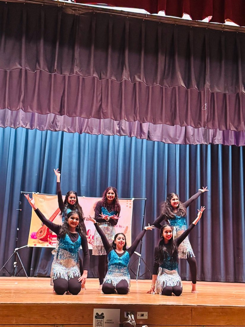 Young dancers in sequined costumes performing on stage at an Oikotaan program