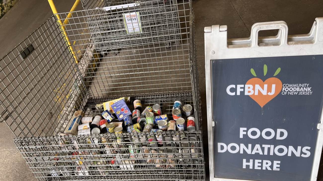 A donation bin overflowing with canned goods next to a Community FoodBank of New Jersey food donations sign