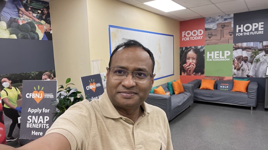 An Oikotaan volunteer at the Community FoodBank of New Jersey, in front of a mural reading Food, Help, Hope