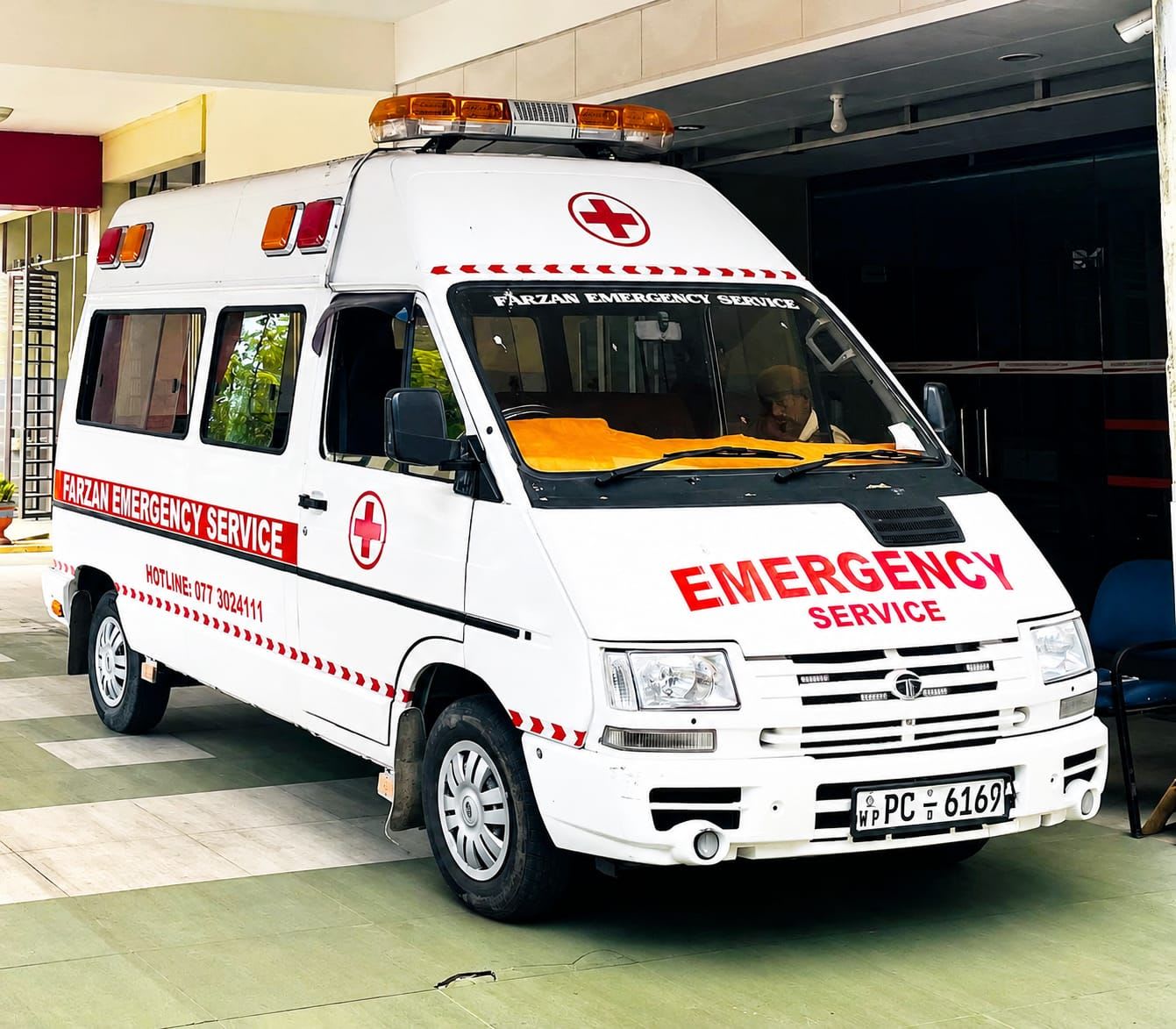 White ambulance with red cross, orange lights, and 'EMERGENCY SERVICE' text.