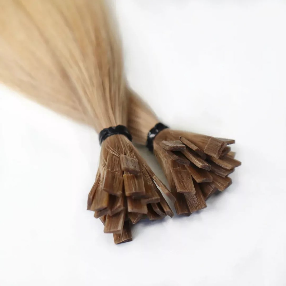 Mèches de cheveux longs et lisses blond châtain, extrémités kératine fixées par anneaux noirs, sur fond blanc.