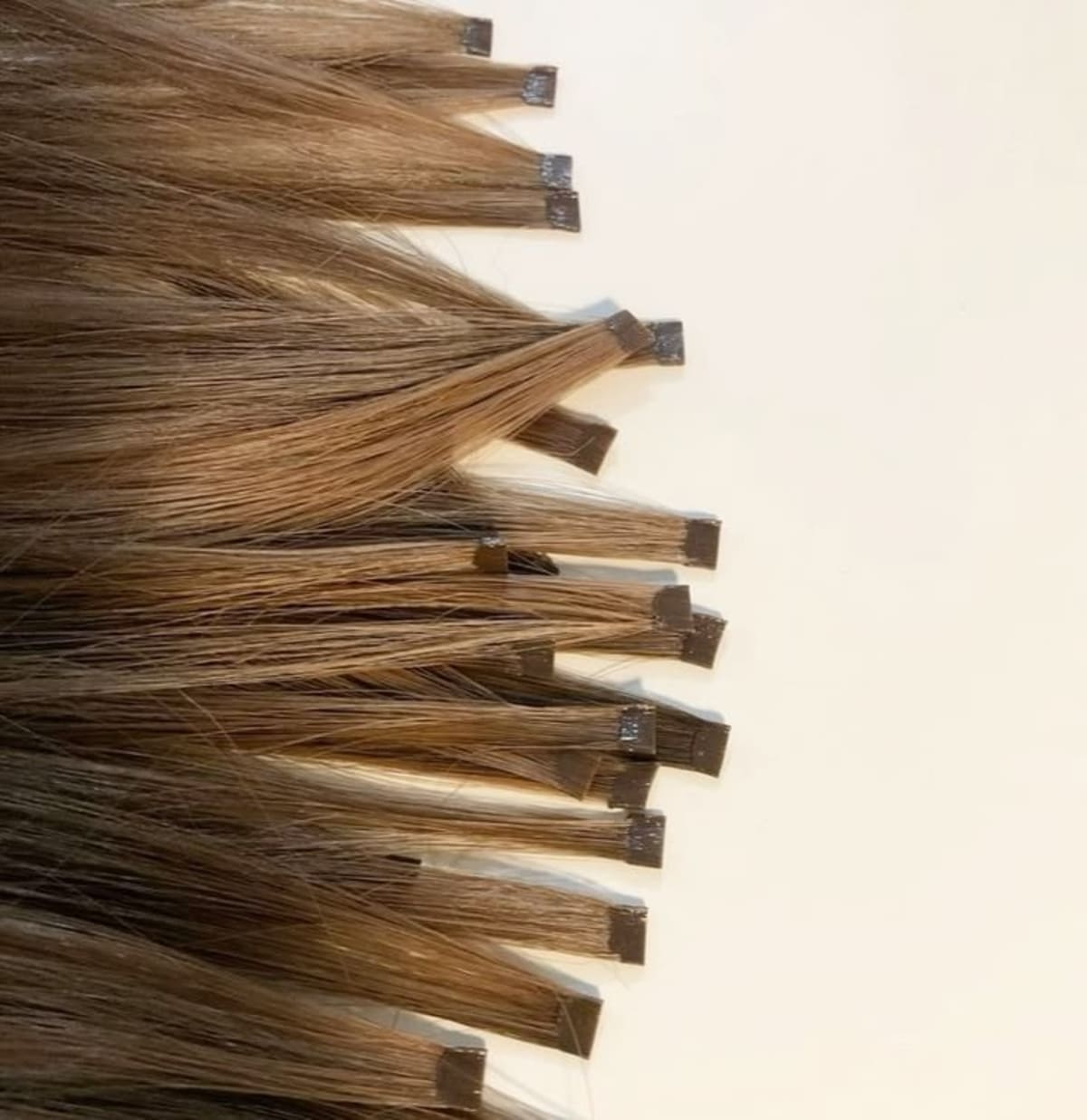 Mèches de cheveux châtain clair, longues et lisses, avec extensions adhésives, sur fond beige uni.