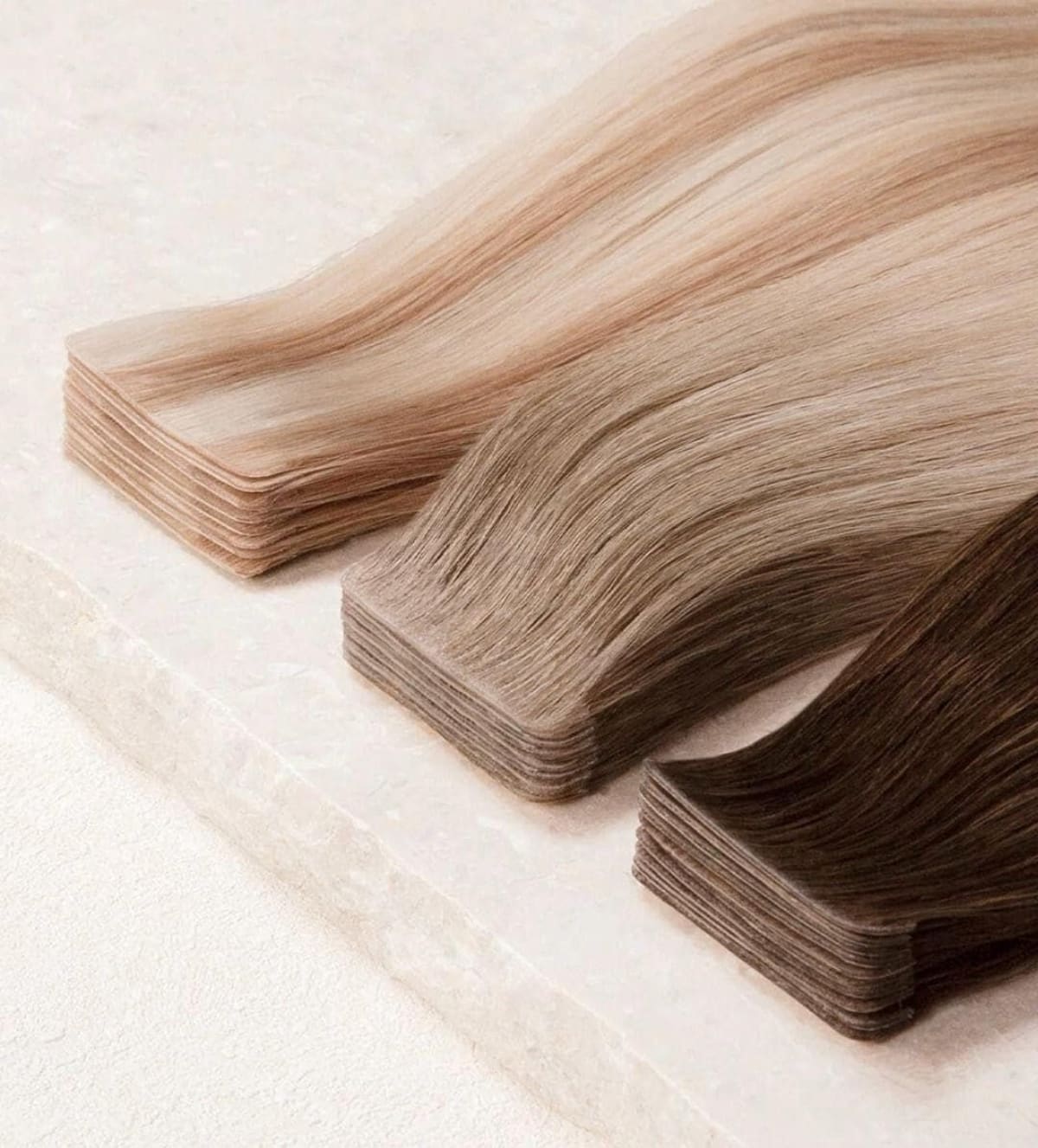 Tape-in extensions i blonda och bruna nyanser lagda bredvid varandra, med tejplagren synliga