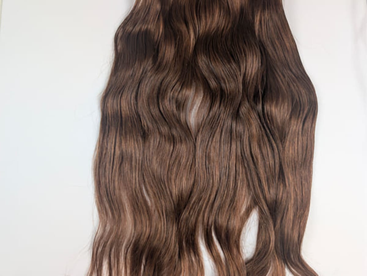 Long wavy brown hair extensions with lighter highlights, laid flat on a white background.