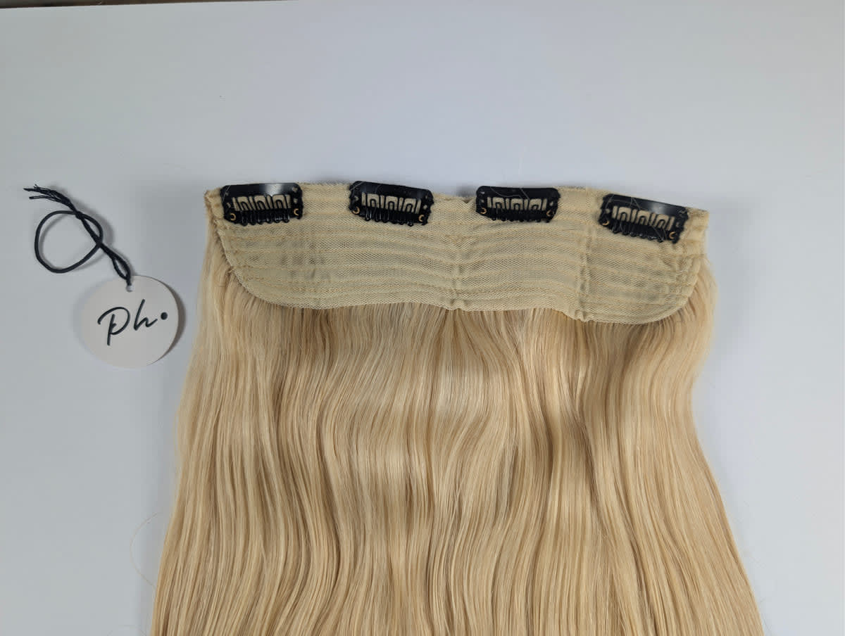 Extension di capelli biondi lunghi e ondulati con quattro clip nere, su sfondo bianco e cartellino rotondo.