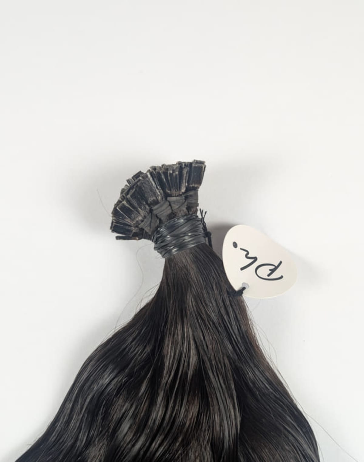 Mèche de cheveux longs et lisses, brun foncé, à kératine plate, avec étiquette ronde attachée, sur fond blanc.