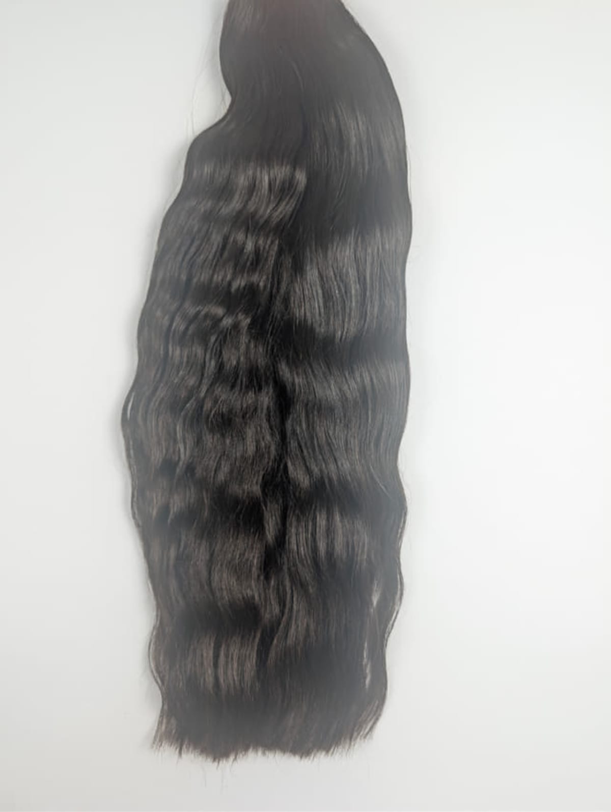 Lange, donkerbruine golvende haarlok hangend tegen een witte achtergrond.