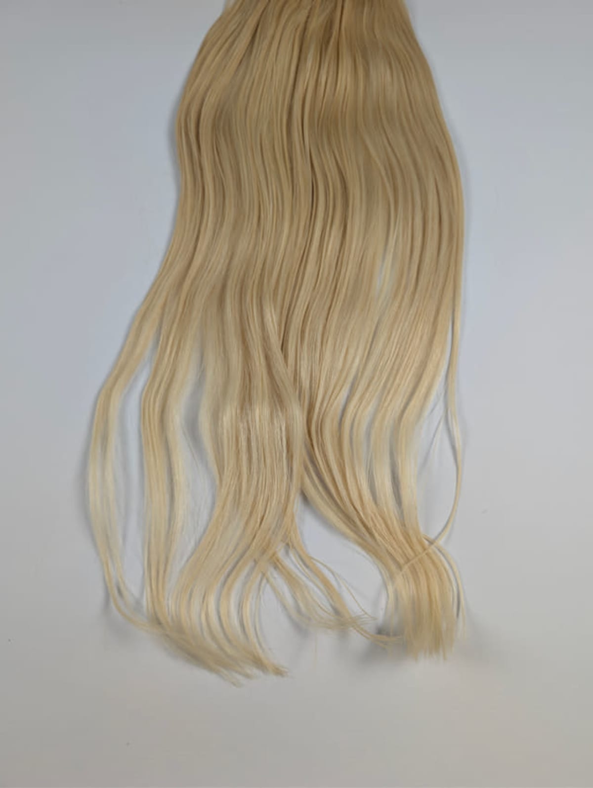 Langes, leicht gewelltes blondes Haar hängt vor grauem Hintergrund.