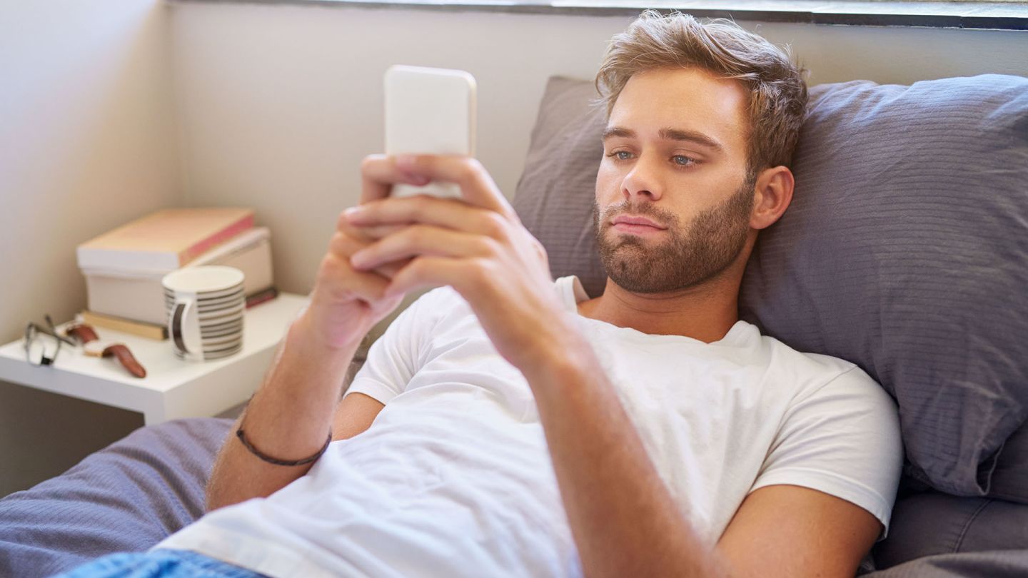 Man lying in bed checking on his phone for how quickly Viagra starts working