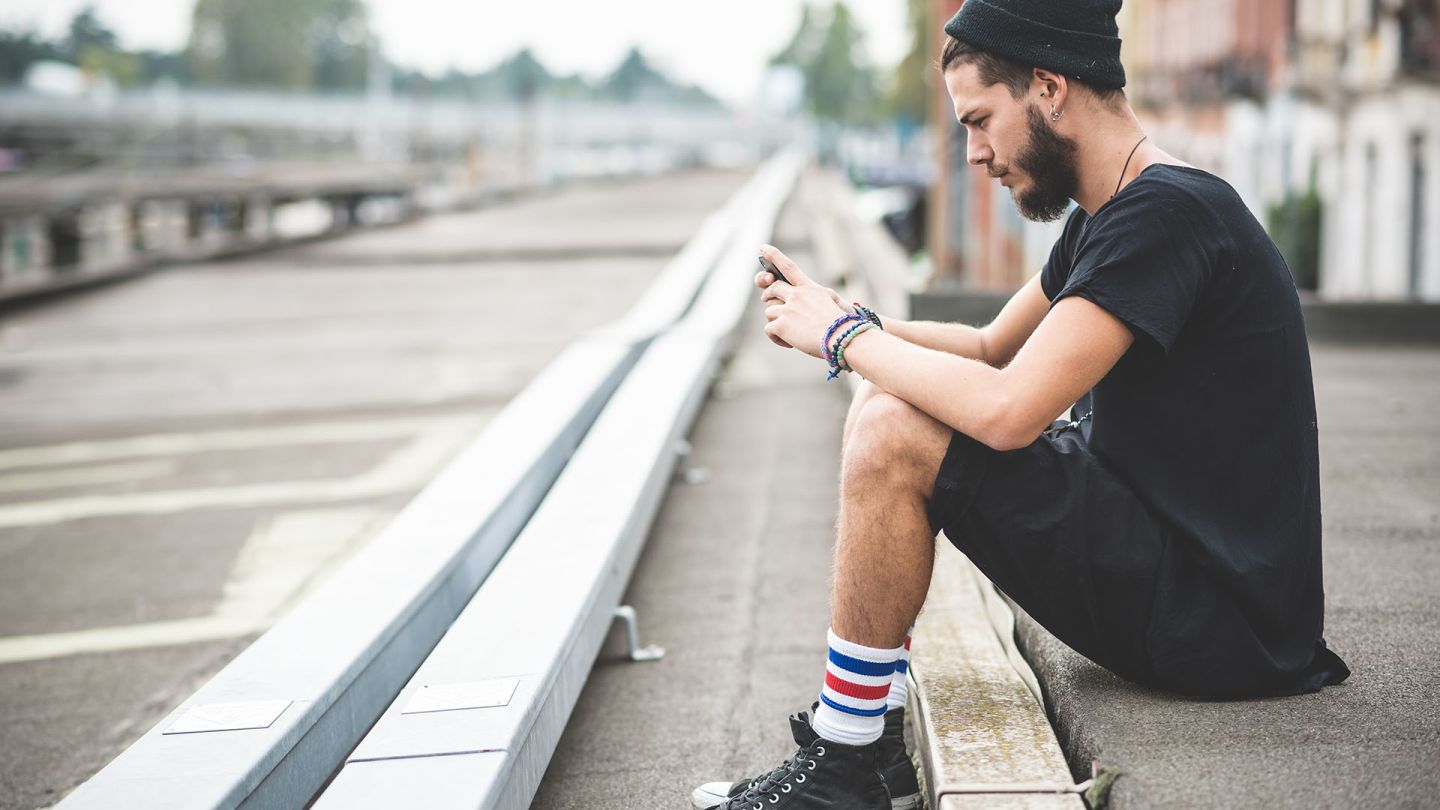 Man sat on the side of a street looking up performance anxiety on his smartphone