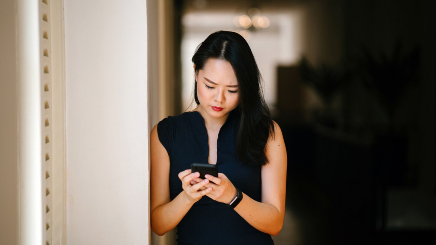 Concerned asian woman leaning against pillar looking up symptoms of hiv in women on mobile