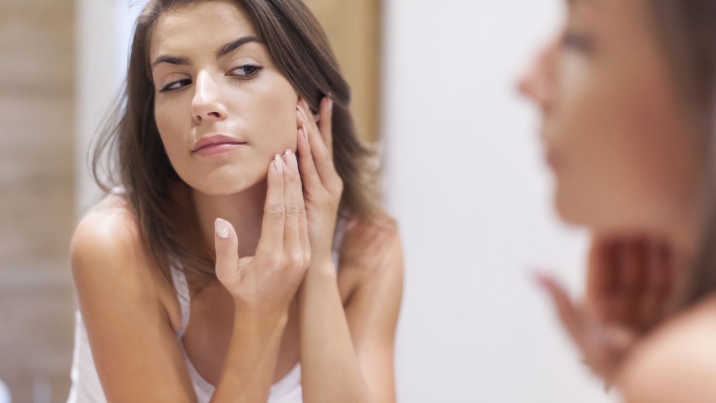 Woman looking in a bathroom mirror checking her face for signs on acne