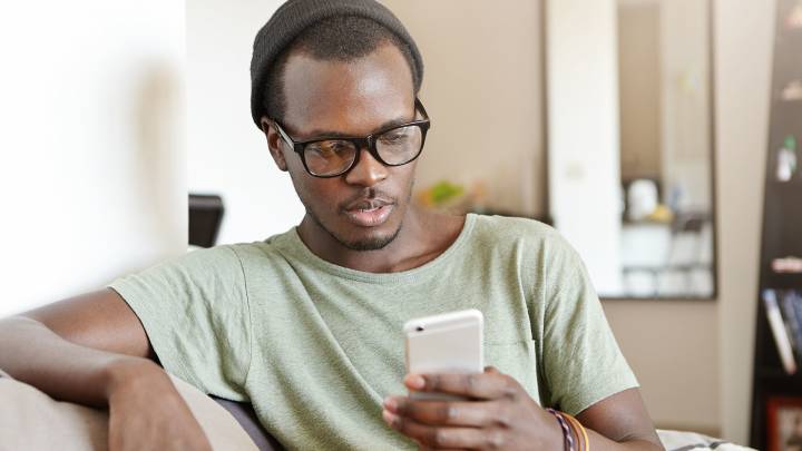 Black man sat on couch at home on phone researching the internet on ways to last longer in bed