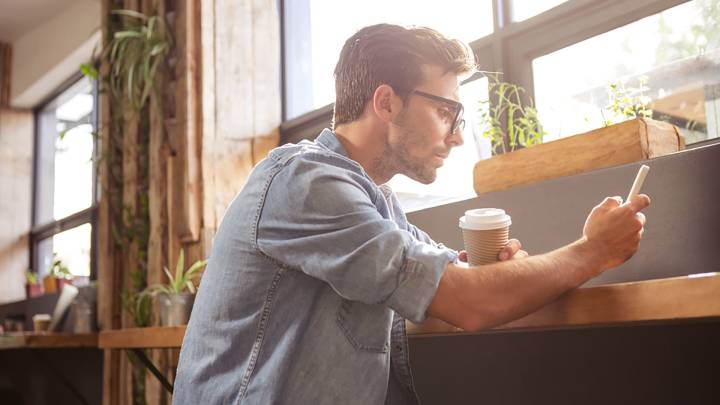 Man sat in cafe holding a coffee and checking his phone for information on erectile dysfunction and diabetes