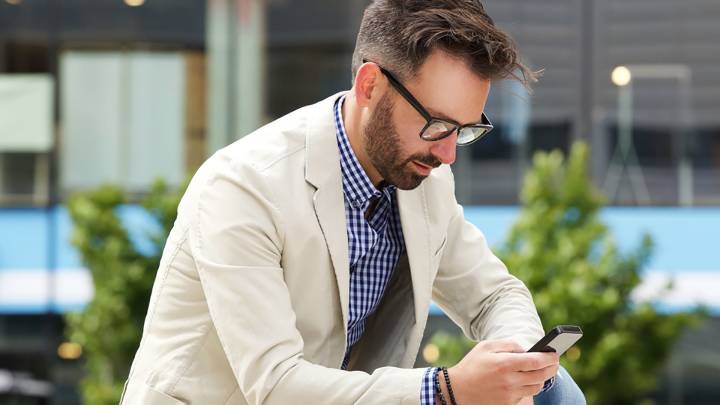 Man wearing glasses sat outside looking up early symptoms of hiv on mobile phone