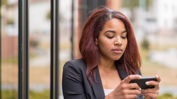 Woman who is stood in front of a building is researching coming off the pill on her phone