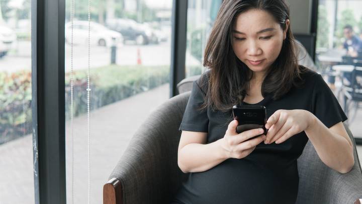 Pregnant woman sat next to a window in a public building looks up chlamydia in pregnancy on her phone