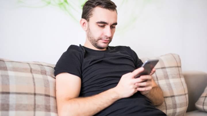 Man sat on couch researching the causes of premature ejaculation on his mobile