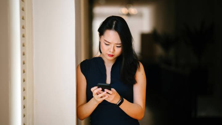 Concerned asian woman leaning against pillar looking up symptoms of hiv in women on mobile