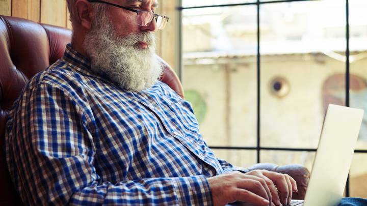 Man sat in a leather chair in front of a window looks up side effects of Lisinopril on his laptop