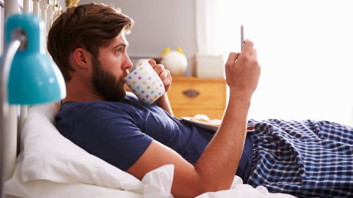 Man looking up painful urination on his phone in bed