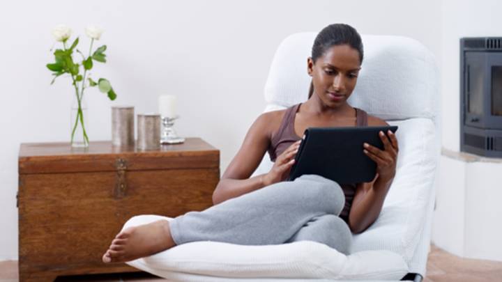 Woman lying in a chair looking up the causes of irregular periods on her tablet