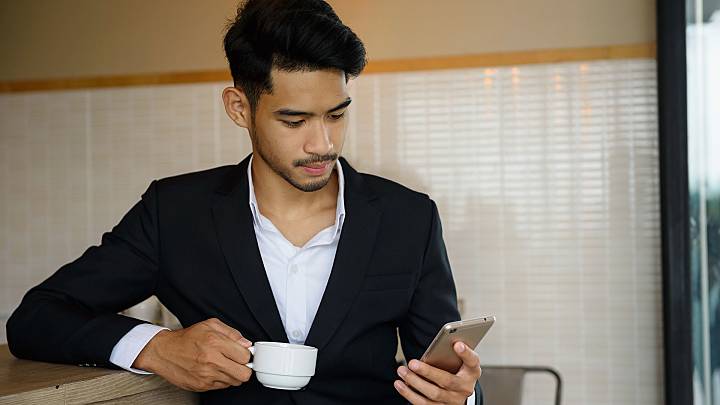 Man in a cafe holding an espresso looking for male enhancement pills on his phone
