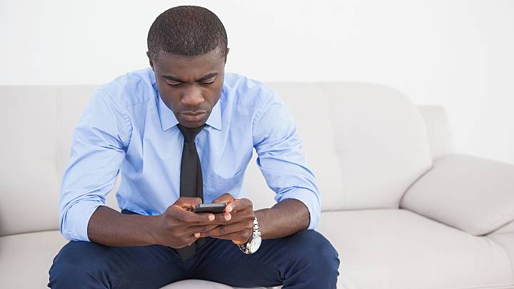 Man sat on a sofa looking up what Kamagra is on his phone