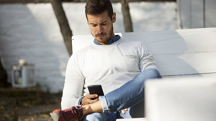 Man sat on a bench in his garden reading about Peyronie's disease on his phone