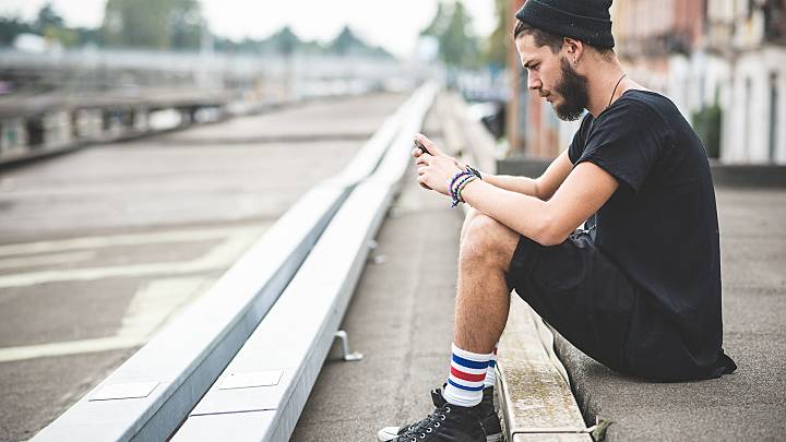 Man sat on the side of a street looking up performance anxiety on his smartphone