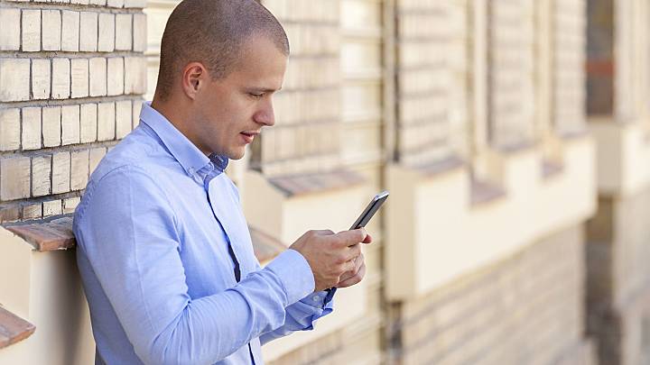 Man outside building typing on mobile phone to see a list of STDs