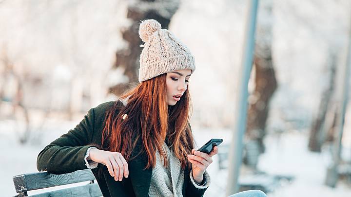 Woman sat on a park bench in the snow is checking her phone for information about contraceptive injections