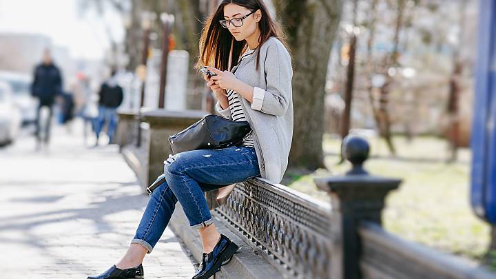 Young woman sat on a bannister outside investigating ways to prevent malaria on her phone