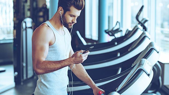 Man at the gym who has stopped using the treadmill looking up exercise induced asthma on his phone