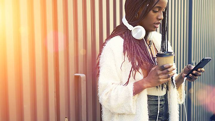 Woman stood in front of a fence holding a coffee and looking up the contraceptive implant on her phone