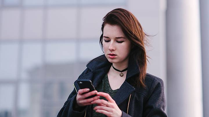 Woman stood in front of a building checking her phone for information about the contraceptive diaphragm