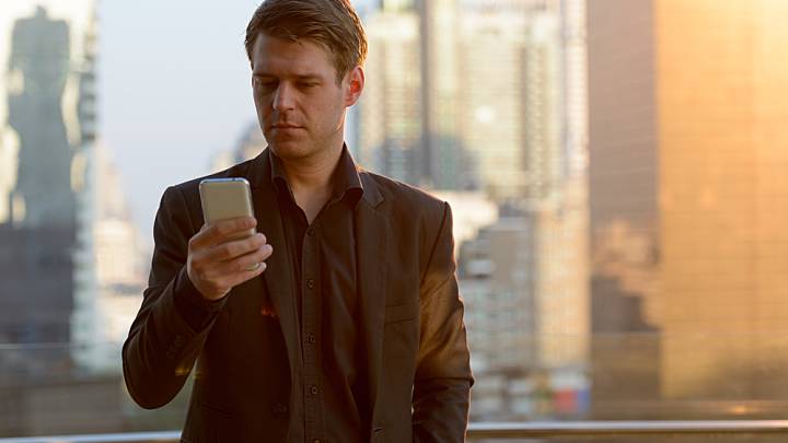 Man stood in front of city skyline checking his phone for tests for erectile dysfunction