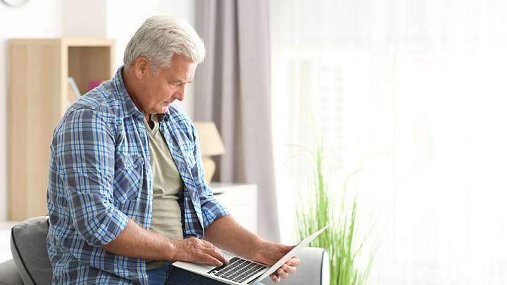 Man sat on the arm of a chair researching the symptoms of high blood pressure on his laptop
