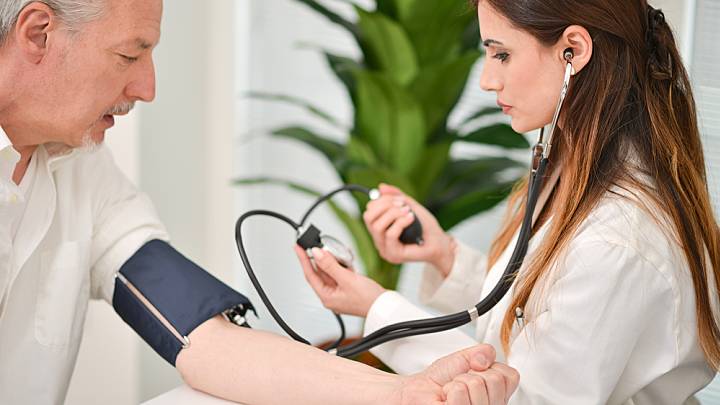 Man at risk of the causes of high blood pressure having his blood pressure check manually by a doctor