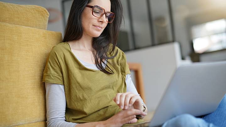 Woman sat on the floor with her back against a chair checks what normal blood pressure is on her laptop