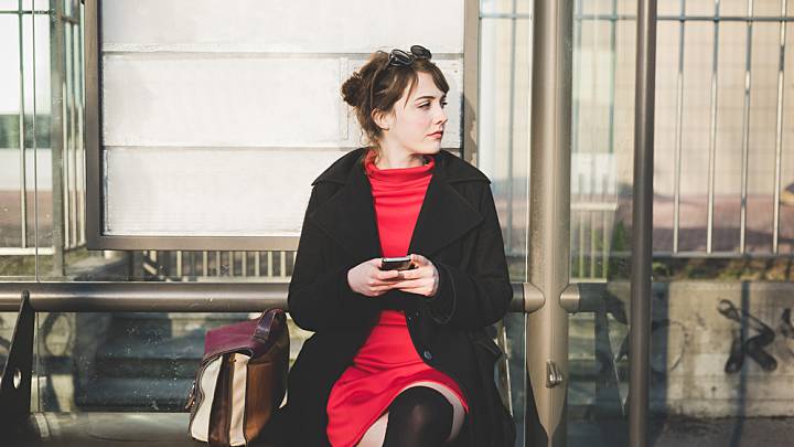 Woman sat at a bus stop is checking on her phone for the symptoms of chlamydia in women