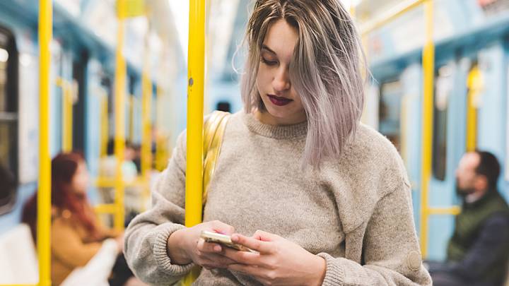 Woman holding onto a pole on an underground train looks up intrauterine contraceptives on her phone
