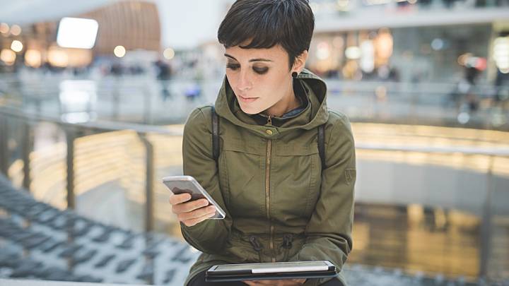 Woman sat in front of a window checking her phone and tablet for information about the pill and antibiotics